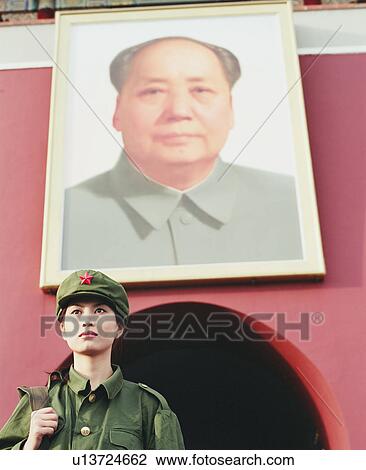 Stock Image - "Low angle view of a young woman in army uniform standing in front of a palace, Forbidden Palace, Beijing, China". Fotosearch