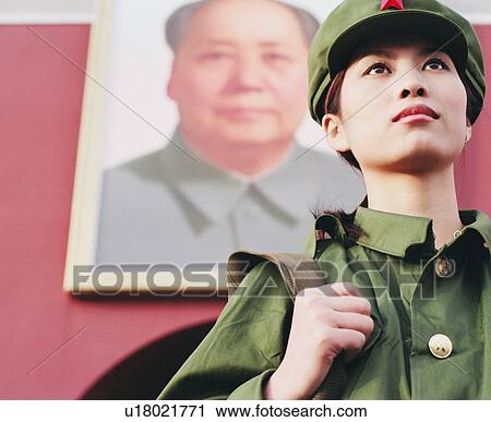 Stock Image - "Low angle view of a young woman in army uniform standing in front of a palace, Forbidden Palace, Beijing, China". Fotosearch