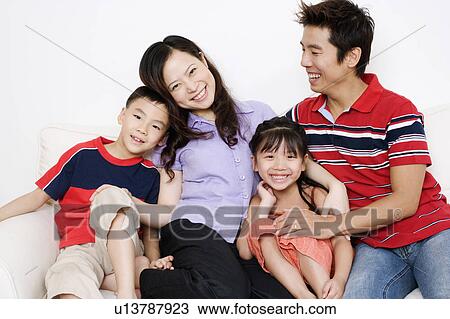 Mid adult man and a young woman sitting on a couch with their son and daughter View Large Photo Image Stock Image - Mid adult man and a young woman sitting on a couch with their son and daughter. Fotosearch