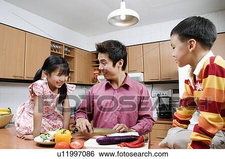 Stock Photograph - Mid adult man and his children cutting vegetables at a kitchen counter. Fotosearch