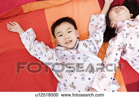 Stock Image - Portrait of a boy lying on the bed and his sister lying beside him. Fotosearch