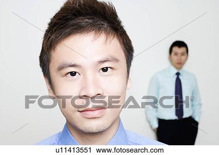 Stock Image - Portrait of a businessman with another standing behind him. Fotosearch