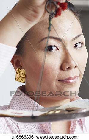 Stock Photograph - Portrait of a businesswoman weighing paper currency with coins on a weighing scale. Fotosearch