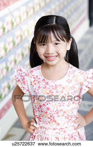 Stock Photo - Portrait of a girl standing with arms akimbo and smiling. Fotosearch