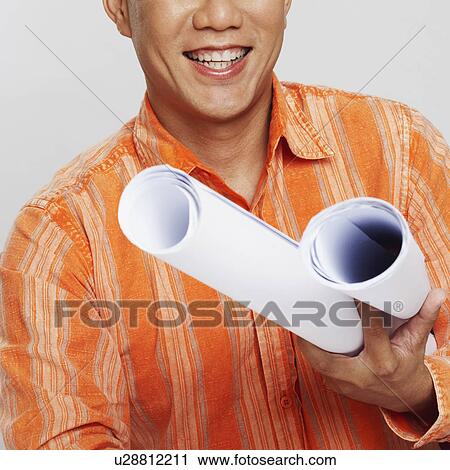 Stock Image - Portrait of a male architect holding two blueprints and smiling. Fotosearch