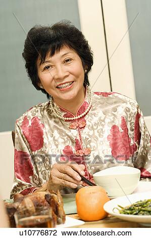 Stock Image - Portrait of a mature woman sitting at the dining table. Fotosearch
