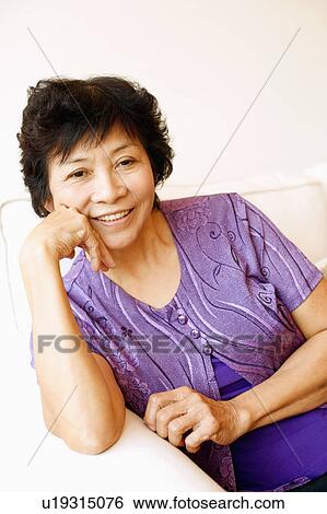 Stock Photograph - Portrait of a mature woman sitting on a couch. Fotosearch