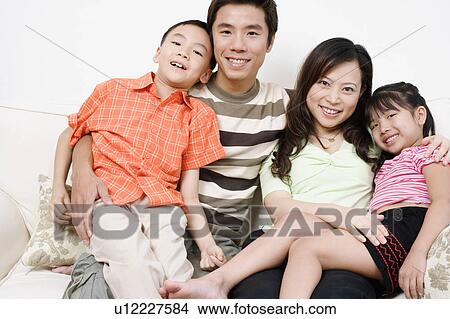 Portrait of a mid adult man and a young woman sitting on a couch with their son and daughter View Large Photo Image Picture - Portrait of a mid adult man and a young woman sitting on a couch with their son and daughter. Fotosearch