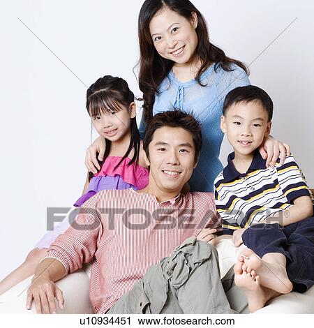 Stock Image - Portrait of a mid adult man and a young woman sitting in an armchair with their son and daughter. Fotosearch