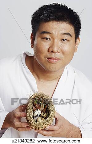 Stock Image - Portrait of a mid adult man holding a bird's nest. Fotosearch