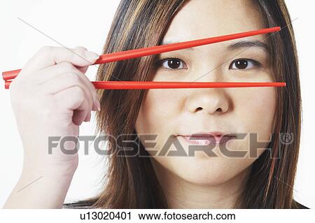 Stock Image - Portrait of a mid adult woman looking through chopsticks. Fotosearch