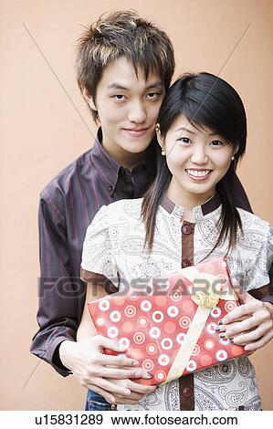 Portrait of a young couple holding a gift and smiling View Large Photo Image Stock Photo - Portrait of a young couple holding a gift and smiling. Fotosearch