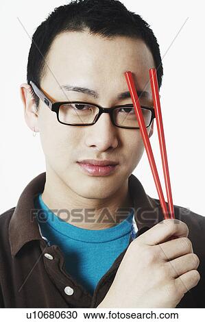 Stock Image - Portrait of a young man holding chopsticks. Fotosearch