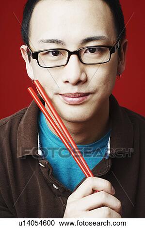 Stock Image - Portrait of a young man holding chopsticks. Fotosearch