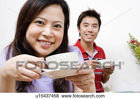 Stock Photo - Portrait of a young woman and a mid adult man drinking tea. Fotosearch