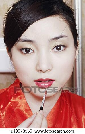 Portrait of a young woman applying lip gloss View Large Photo Image Stock Photo - Portrait of a young woman applying lip gloss. Fotosearch
