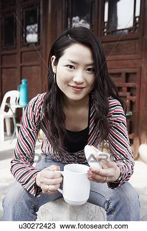 Stock Image - Portrait of a young woman holding a mug with a lid smiling. Fotosearch