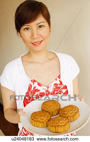Stock Image - Portrait of a young woman holding a plate of cake. Fotosearch