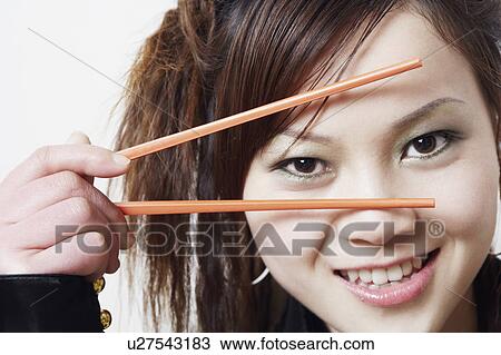 Stock Image - Portrait of a young woman holding a pair of chopsticks. Fotosearch