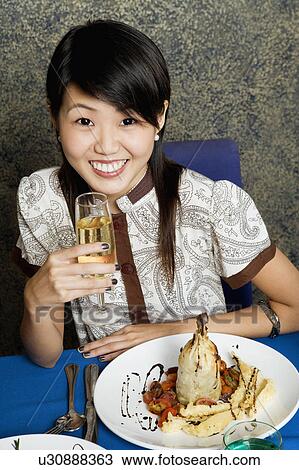 Stock Image - Portrait of a young woman holding a glass of champagne and smiling. Fotosearch