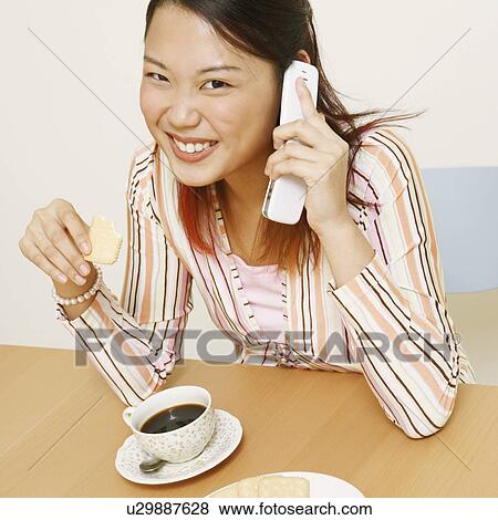Portrait of a young woman holding a cookie and talking on a mobile phone View Large Photo Image Stock Photo - Portrait of a young woman holding a cookie and talking on a mobile phone. Fotosearch