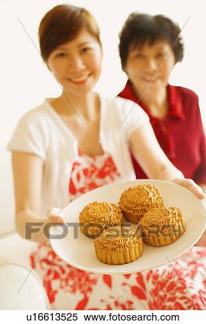 Stock Photography - Portrait of a young woman holding a plate of cake with her mother back. Fotosearch