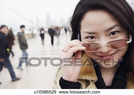 Portrait of a young woman holding sunglasses over her eyes View Large Photo Image Stock Photo - Portrait of a young woman holding sunglasses over her eyes. Fotosearch