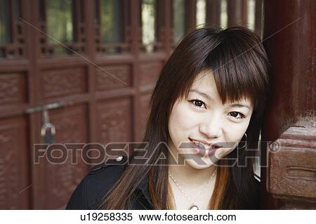 Stock Photography - Portrait of a young woman leaning against a column smiling. Fotosearch
