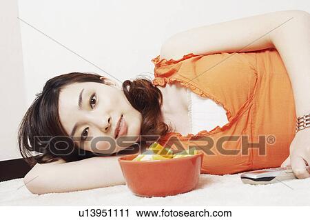 Stock Image - Portrait of a young woman lying down holding a mobile phone. Fotosearch