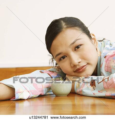 Stock Image - Portrait of a young woman lying in front of a tea cup. Fotosearch