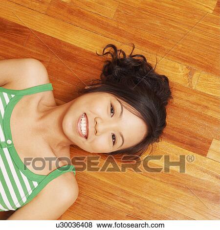 Stock Photo - Portrait of a young woman lying on a hardwood floor and holding a mobile phone. Fotosearch