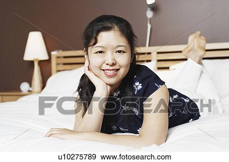 Portrait of a young woman lying on the bed thinking with her hand on her chin View Large Photo Image Stock Photo - Portrait of a young woman lying on the bed thinking with her hand on her chin. Fotosearch
