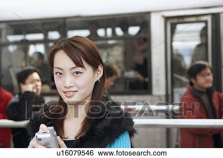 Stock Photograph - Portrait of a young woman operating a mobile phone with a digitized pen. Fotosearch