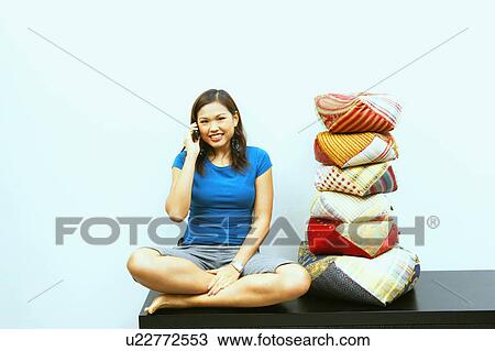 Portrait of a young woman sitting on a cabinet and talking on a mobile phone View Large Photo Image Stock Image - Portrait of a young woman sitting on a cabinet and talking on a mobile phone. Fotosearch