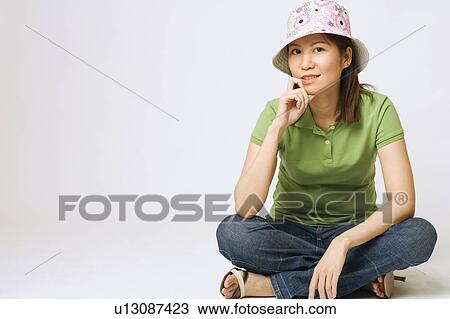 Stock Image - Portrait of a young woman sitting with her hand on her chin. Fotosearch