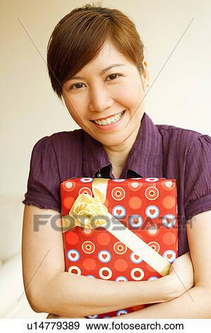 Stock Photo - Portrait of a young woman smiling and holding a gift. Fotosearch