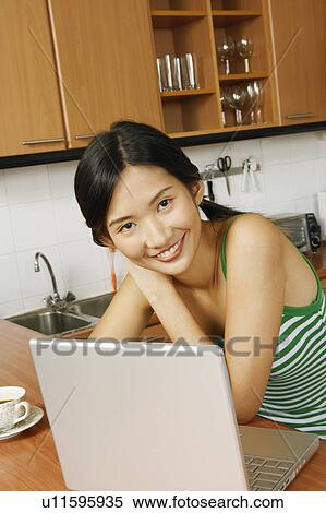 Portrait of a young woman smiling in front of a laptop at a kitchen counter View Large Photo Image Stock Photography - Portrait of a young woman smiling in front of a laptop at a kitchen counter. Fotosearch