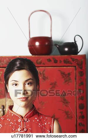 Stock Image - Portrait of a young woman standing in front of a cupboard. Fotosearch