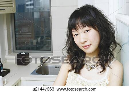 Stock Image - Portrait of a young woman standing in the kitchen smiling. Fotosearch