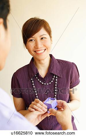 Stock Image - Rear view of a young man offering a ring to a young woman. Fotosearch