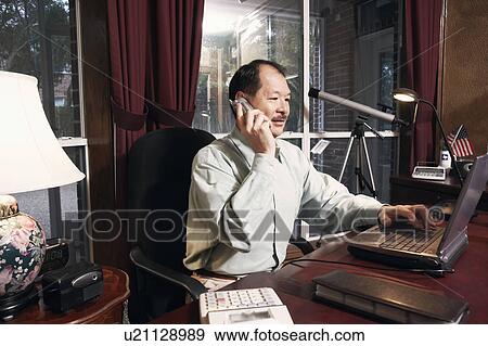 Senior man using a laptop talking on a cordless telephone View Large Photo Image Stock Photo - Senior man using a laptop talking on a cordless telephone. Fotosearch