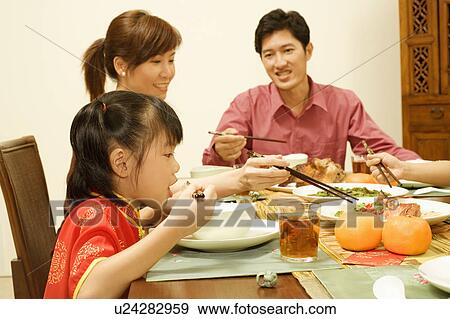 Stock Photo - Side profile of a girl sitting at the dining table with her parents. Fotosearch