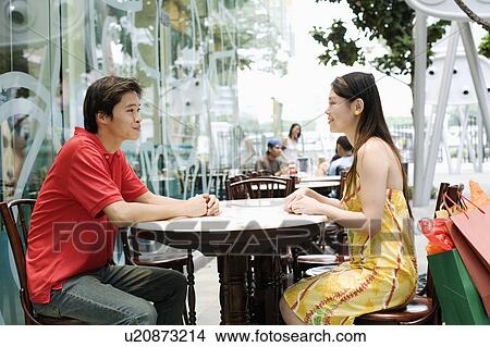 Side profile of a young couple sitting in a cafeteria View Large Photo Image Picture - Side profile of a young couple sitting in a cafeteria. Fotosearch