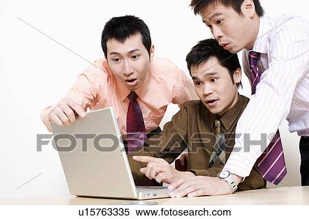 Stock Photography - Three businessmen using a laptop and looking surprise. Fotosearch