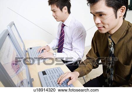 Stock Image - Two businessmen working on computers. Fotosearch