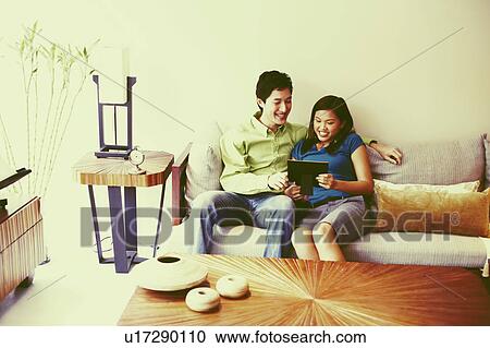 Young couple looking at a picture frame and smiling on a couch View Large Photo Image Stock Image - Young couple looking at a picture frame and smiling on a couch. Fotosearch