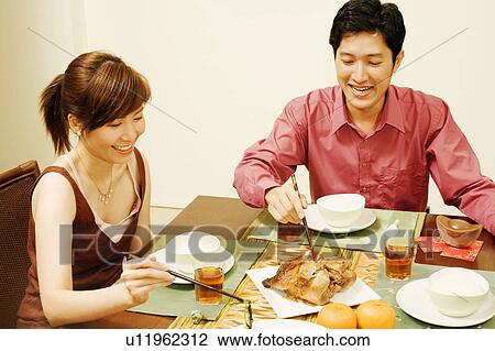 Stock Image - Young couple sitting at the dining table and eating food. Fotosearch