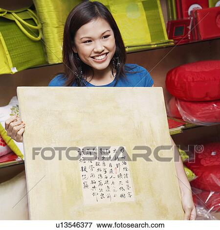 Stock Photo - Young woman holding a painting in a store. Fotosearch