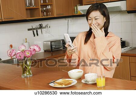Young woman looking at a mobile phone at a kitchen counter View Large Photo Image Stock Image - Young woman looking at a mobile phone at a kitchen counter. Fotosearch
