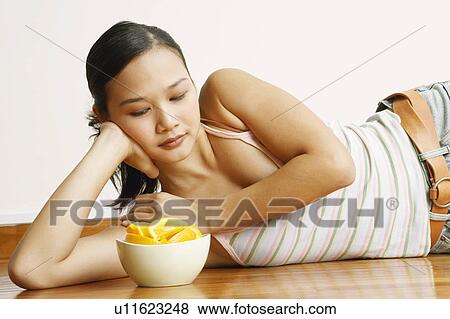 Stock Photo - Young woman lying on the floor with a bowl of orange slices in front of her. Fotosearch